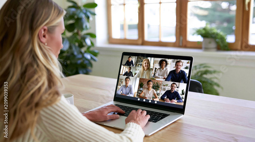 Blonde woman attending a virtual video conference on a laptop from a bright home office, connecting with a diverse remote team in an online meeting, highlighting modern communication and