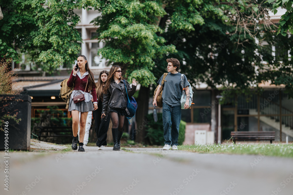 Obraz premium A group of high school students walk together outdoors carrying backpacks and chatting. Four teenagers stroll across a school campus in casual clothing between classes.