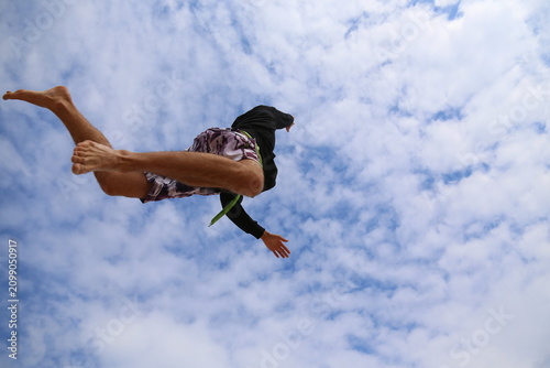 Athletic young man jumping upward on beach with arms extended, dynamic action