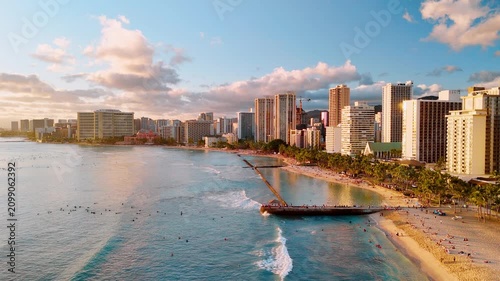 Aerial view of Waikiki beach with surfer, Honolulu, Hawaii. Turquoise wave, sandy shore, pier and hotel tower at golden hour.
