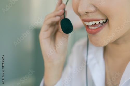A smiling Asian female call center agent wearing a headset and speaking with a customer, set against an office background.