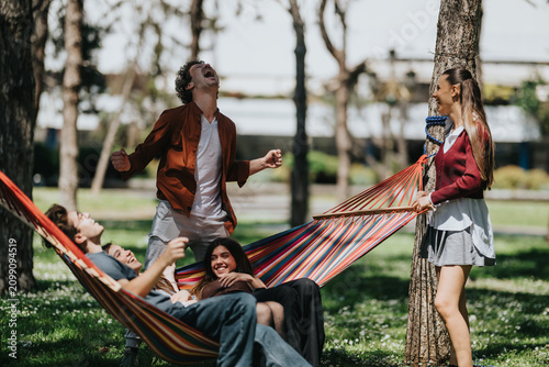Cuadro en lienzo A group of young friends relaxing and laughing in a striped hammock between trees