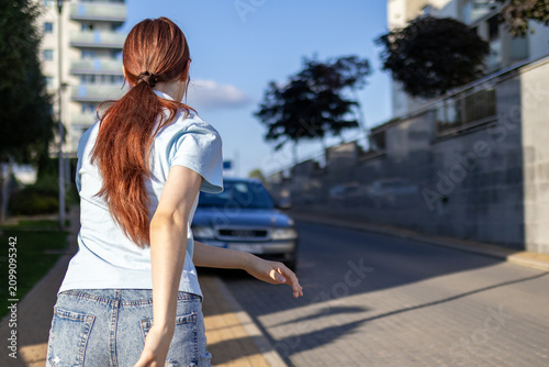 Konstfotografi Red haired teenage girl roller skates along quiet residential street surrounded by modern apartment buildings on sunny summer evening