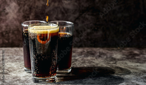 Foto Cold Dark Carbonated Soda Pouring into Glass with Fizzing Bubbles on Dark Stone