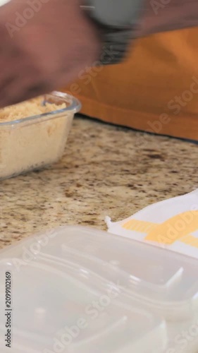 Vertical video: Scooping rice, man in orange packing meals on granite counter for meals, copy space