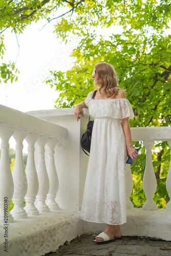 Canvastavla Woman standing near white railing surrounded by green trees in a garden while ho