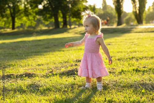 happy little girl in a pink dress walks in the park at sunset. A toddler walking outdoors exploring the world around her.