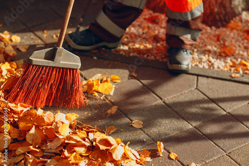 Fotografie Janitor cleaner sweeping off autumn leaves and garbage trash on the street walkway