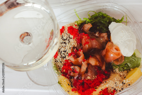 Seafood bowl with rice and vegetables and glass of white wine. Wineglass and fish poke. Fresh food to go. Salmon with salad close up. Seafood restaurant menu. Seafood box with cream cheese.