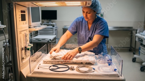 A medical professional prepares a neonatal incubator with blankets and equipment in a hospital setting.