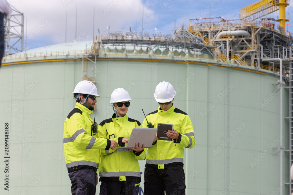 Fototapeta premium Engineers collaborating on construction project at industrial site with laptop and tablet in hand under blue sky