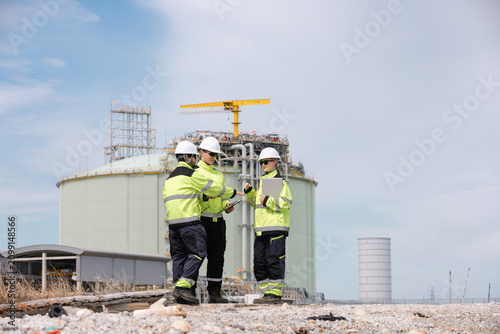 Engineers discussing project plans at a construction site with industrial equipment in the background