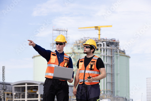 Two engineers discussing construction plans at a modern industrial site with safety gear and equipment