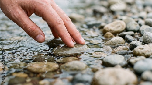 Hand gently touching a wet stone in a shallow creek