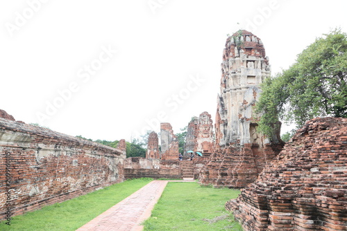 Konstfotografi Ancient Ruins in Thailand: Weathered brick walls and a crumbling stupa stand as testaments to a bygone era, with lush green grass carpeting the ground beneath a hazy sky