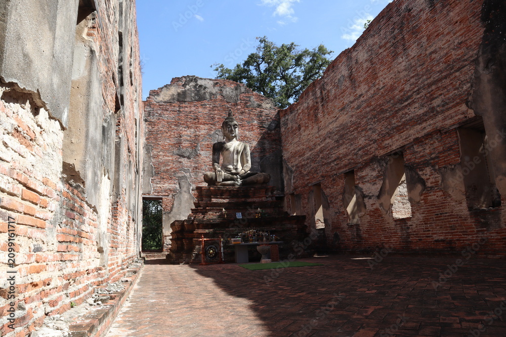 Fototapeta premium Ancient Buddha Statue in Ruined Temple: A serene Buddha statue sits at the heart of a crumbling ancient temple, its brick walls weathered by time.