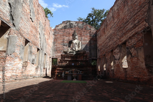 Fotografie Ancient Buddha Statue in Ruined Temple: A serene Buddha statue sits enthroned amidst the crumbling brick walls of an ancient temple, a testament to time and devotion