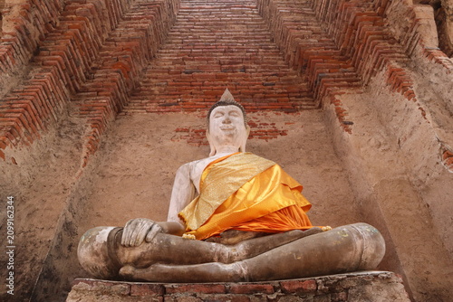 Foto Serene Buddha Statue in Ancient Temple: A serene Buddha statue, adorned with golden robes, sits in a meditative pose within the weathered ruins of an ancient temple
