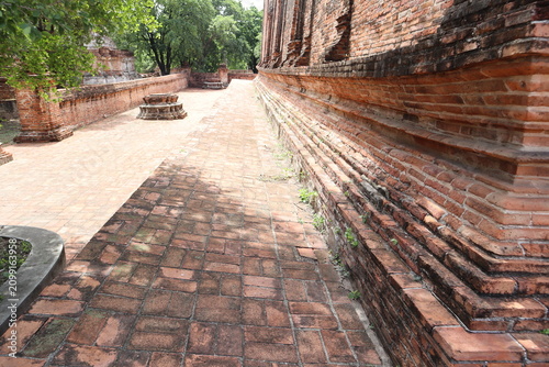 Принти на полотні Ancient Temple Walkway: An ancient brick walkway leads past a weathered brick wall of a temple, with dappled sunlight creating patterns on the ground