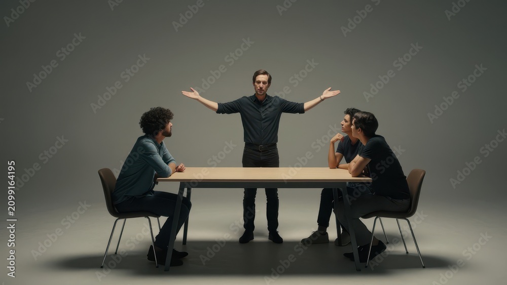 Obraz premium Three young professional colleagues discussing ideas during a meeting with a male leader gesturing with open hands in a minimalist studio setting with dramatic lighting and copy space