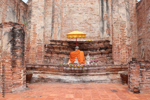 Monk at Ancient Temple Altar: A solitary monk, clad in vibrant orange robes, meditates before an ancient altar in a crumbling temple, illuminated by a golden umbrella.