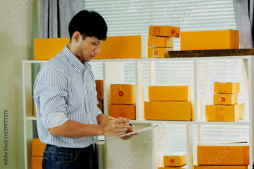 Konstfotografi Smart Asian merchant cross-checking item lists with clipboard to maintain optimal SME warehouse supply