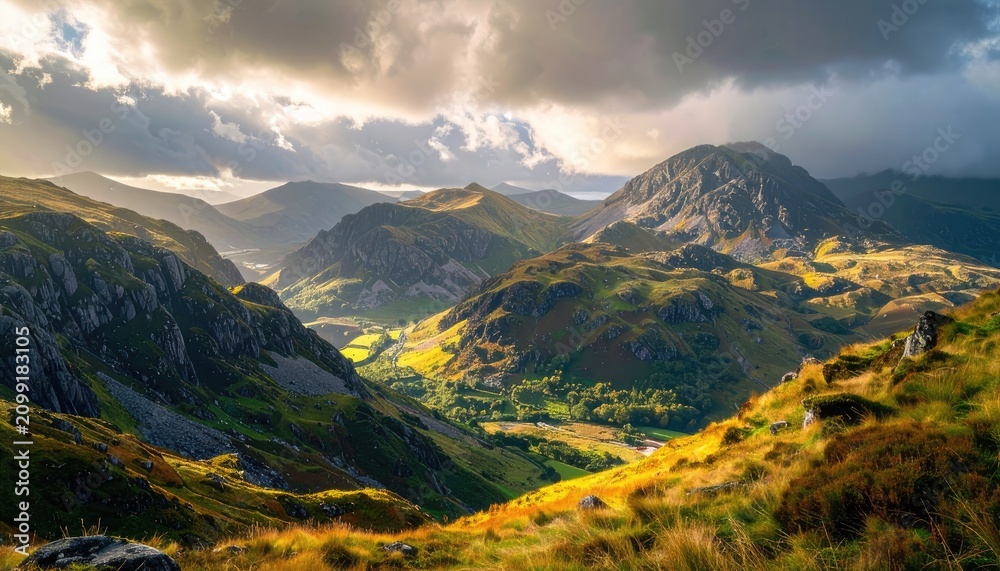 Fototapeta premium Sunlight breaks through clouds over a rugged mountain valley.