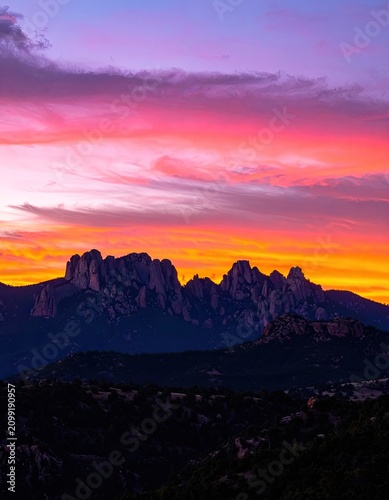 Dramatic sunset paints the sky with vibrant hues over jagged mountain peaks.