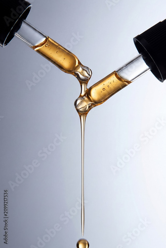 Golden Cosmetic Serum Dripping from Glass Dropper Macro Isolated on Light Background.