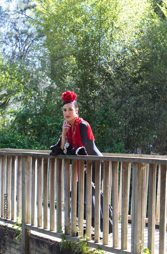 A beautiful woman dancing flamenco, leaning on a wooden railing in Seville. She is wearing a black gypsy dress with ruffles and a flower in her hair. Flamenco, a UNESCO Intangible Cultural Heritage.