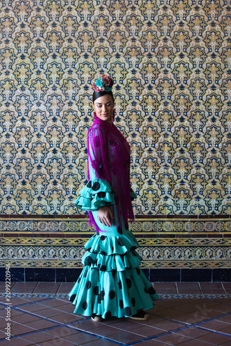 A beautiful woman dancing flamenco in a square in Seville, Spain. She is wearing a turquoise dress with black polka dots and a flower in her hair. Flamenco, a UNESCO Intangible Cultural Heritage.