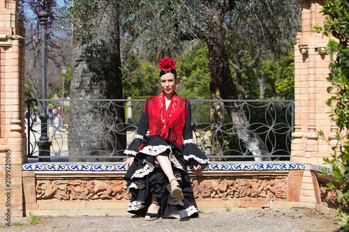 A beautiful flamenco dancer sitting on a tiled bench in a square in Seville, Spain. She is wearing a black ruffled dress and a shawl. Flamenco, a UNESCO Intangible Cultural Heritage.
