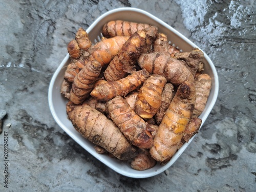 Bild auf Leinwand Fresh turmeric rhizomes piled in a white bowl on a rustic concrete background, highlighting a natural spice widely used in cooking, herbal medicine, and healthy nutrition