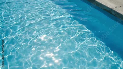Clear blue water ripples in a sunny swimming pool. Surface of liquid moving gently in resort basin. Summer vacation relaxation and refreshing aquatic background.
