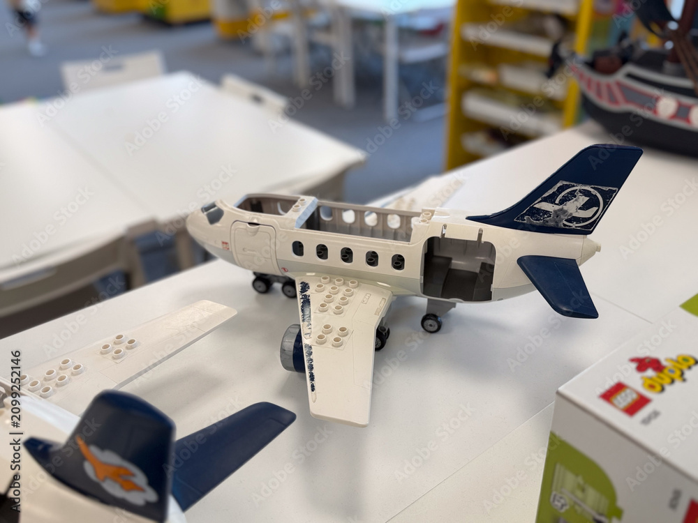 Fototapeta premium Lego-style toy airplane model on a table in a classroom or workshop, with blurred building area in the background