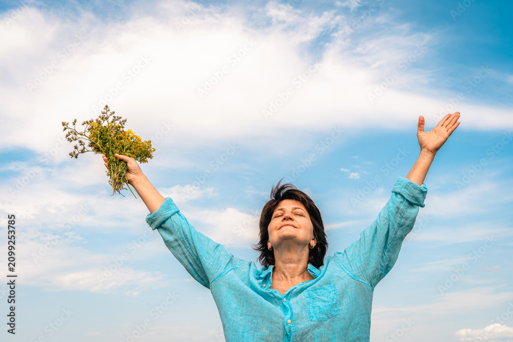Obraz premium Woman standing in green field with her arms outstretched, facing sun, embracing happiness and beauty of nature. Women's mental health, accepting one's age