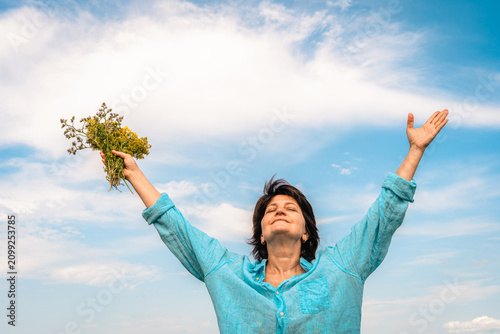 Woman standing in green field with her arms outstretched, facing sun, embracing happiness and beauty of nature. Women's mental health, accepting one's age