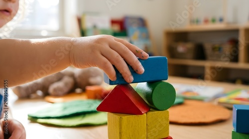 A young child s hand carefully stacks colorful geometric wooden building blocks developing fine motor skills and spatial reasoning while playing with educational toys in a bright engaging