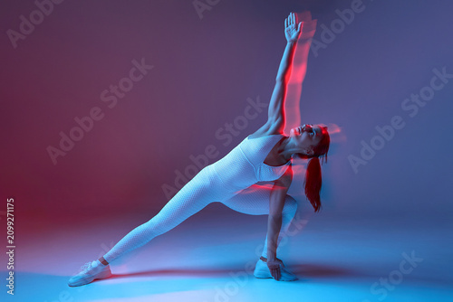 woman practicing yoga in side plank pose with energetic and focused expression against studio gradient background, white athletic outfit, fabric of yoga mat, modern and clean visual space.