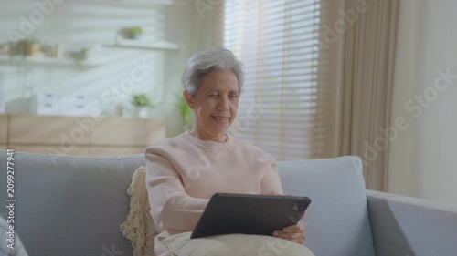 Older asian woman using tablet sitting relaxed on couch at home, smile or laugh with happy time. enjoy watch or read text on social media app. Senior asian with digital technology after retired.
