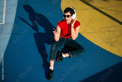 Woman enjoying music with headphones and smartphone on colorful court