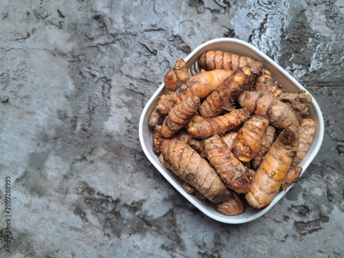 Bild auf Leinwand Fresh turmeric rhizomes in a white bowl on a rustic concrete background with copy space, showcasing a natural spice for cooking, herbal remedies, and healthy nutrition