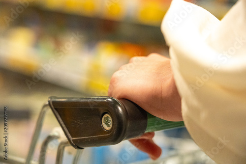 A Close-Up of a Hand Grasping a Shopping Cart Handle in a Supermarket Aisle Filled with Colorful Products and Groceries Ready for Selection