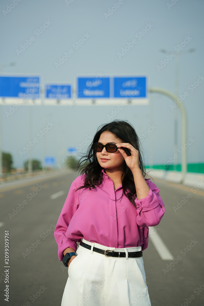 Fototapeta premium Woman adjusts sunglasses while standing confidently on an open highway