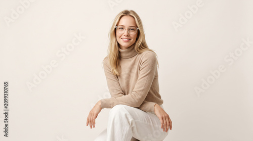 Confident Young Blonde Woman in Beige Turtleneck and Eyeglasses Smiling for Studio Portrait