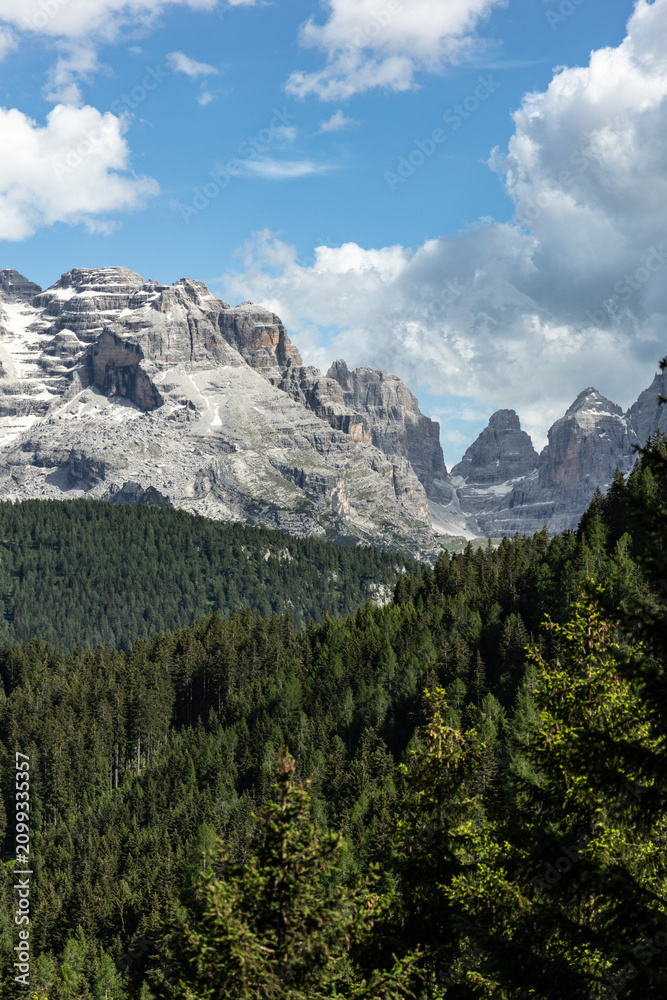 Fototapeta premium Dolomite mountain peaks above evergreen forest under dramatic clouds in Italy