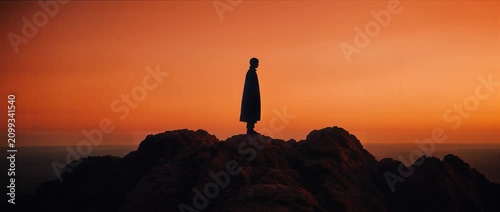 Silhouette of a lone person standing on a rocky mountain peak at sunset