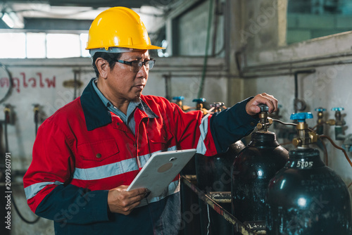 Technician hard hat gas cylinder tablet inspection factory safety worker male technician in red uniform checking industrial gas cylinder valve