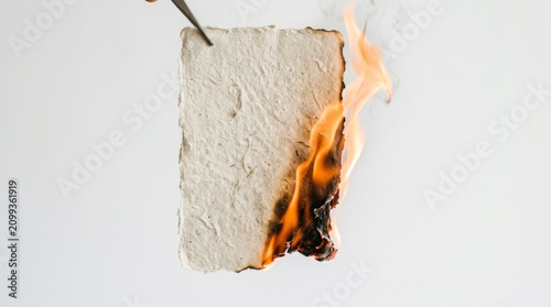 Handmade paper burning on white background. Texture sheet catching fire for creative design.