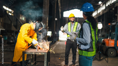 Factory worker welding helmet safety vest industrial metal spark workshop construction, team working in warehouse with protective gear and machinery